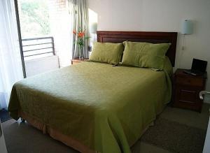 a bedroom with a large bed with green sheets and a window at Lobato Apartments in Santiago