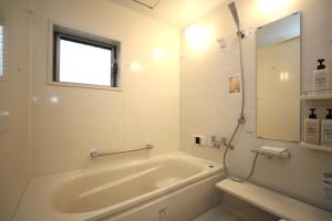 baño blanco con bañera y ventana en 一棟貸切り宿 GuestHouse 嵯峨嵐山, en Kioto