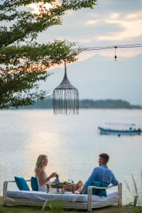 un homme et une femme assis à une table près de l'eau dans l'établissement The Beach House Resort, à Gili Trawangan