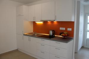 a kitchen with white cabinets and an orange wall at Apartments with a parking space Nerezine, Losinj - 15768 in Nerezine