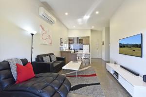 a living room with a black leather couch and a tv at Ironbark Hill Villa 1 Tyrian in Pokolbin