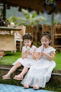 twee kleine meisjes in witte jurken die ijs eten bij Trang An Bungalow in Ninh Binh