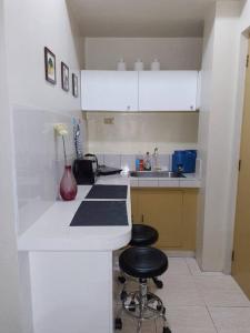 a white kitchen with two stools at a counter at Budget Friendly Condo for Rent in Valley Mansions in Cainta