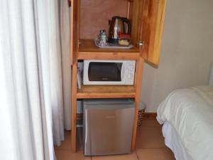 una mesa pequeña con microondas en un estante junto a una cama en The Riverhouse Guesthouse, en Estcourt 18 fotos más