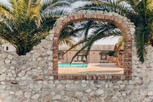 a brick wall with a swimming pool and palm trees at Agriturismo Posta Guevara in Castelluccio dei Sauri