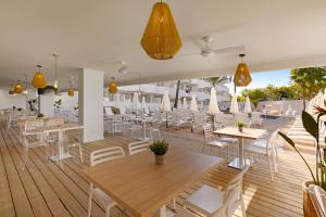 un restaurante con mesas y sillas blancas en una terraza de madera en Palmanova Beach Apartments by TRH en Palmanova