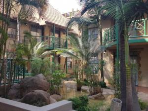 un edificio con palmeras y un estanque frente a él en Court Classique Suite Hotel, en Pretoria