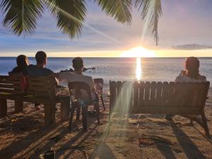 a group of people sitting on a bench watching the sunset at Sunny Beach Bungalows - Aitutaki in Amuri