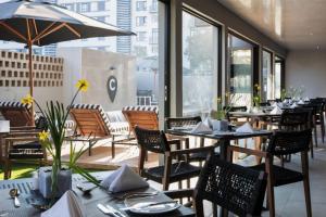 un restaurante con mesas, sillas y ventanas en The Capital Melrose en Johannesburgo