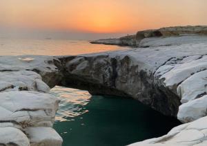 a hole in the rocks in the water with the sunset at Governors Beach Costas Apts in Governor's Beach