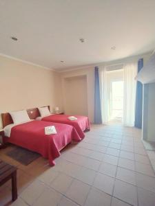 a bedroom with two beds with red sheets and a window at Residência D'Atalaia in Fronteira