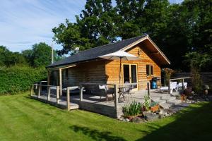 Cabaña de madera con terraza y sombrilla en Acksea Holiday Lodges, en Kinnerley