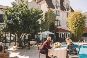 Un uomo e una donna seduti a un tavolo vicino a una piscina di The Elite - Oradea's Legendary Hotel a Oradea