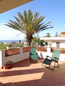 - deux chaises sur une terrasse avec un palmier dans l'établissement La finestra sul mare, à Castellammare del Golfo