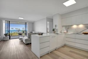 a kitchen with white cabinets and a living room at Panoramic Ocean View 2 bed 2 bath in Alexandra Headland