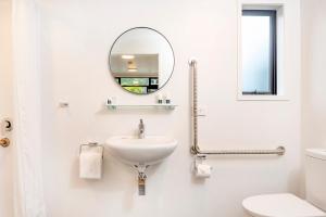 a white bathroom with a sink and a mirror at The Com Plex Motel in Whakatane