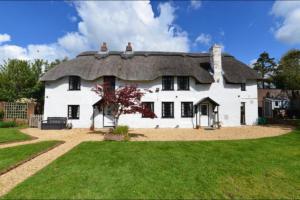 a large white house with a thatched roof at April Cottage, luxurious accommodation for coast and forest with pool & hot tub in Hordle