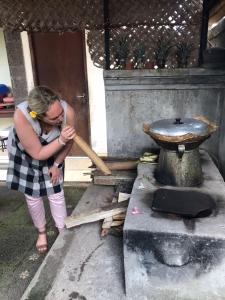 uma mulher segurando um taco de beisebol ao lado de um fogão em Arsa Wayan Guest House em Klungkung