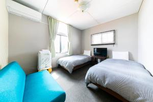 a bedroom with two beds and a blue couch at Guesthouse leaf in Hokuto