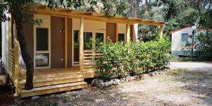 ein kleines Haus mit einer Veranda und einigen Büschen in der Unterkunft Camping Kozarica Mobile Homes in Pakoštane