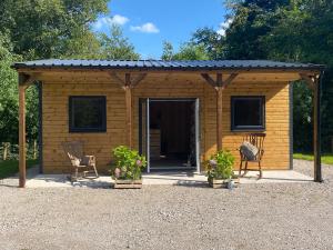 a wooden shed with a roof and two chairs at Kingfisher Cabin - Wild Escapes Wrenbury off grid glamping - ages 12 and over in Baddiley