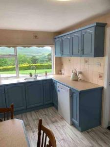 une cuisine avec des placards bleus, un évier et une fenêtre dans l'établissement Mountain House Omeath near Carlingford, à Ó Méith