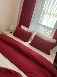 ein rotes und weißes Bett mit roten Kissen und einem Fenster in der Unterkunft Elif Apartman in Novi Pazar