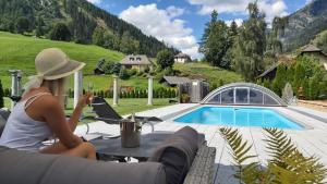 a woman sitting at a table with a laptop next to a pool at Ferienwohnung Aigner im Salzburger Lungau in Muhr
