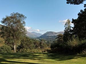 a green field with trees and mountains in the background at Lochs Lodge, Glenlyon, Perthshire 