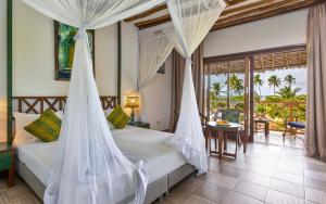 a bedroom with a bed with mosquito nets and a table at Zanzibar Queen Hotel in Matemwe