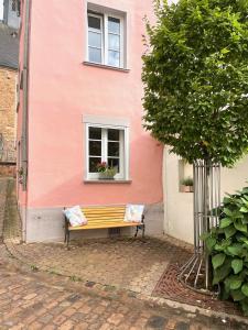 薩爾堡的住宿－Uriges Ferienhaus in der Altstadt von Saarburg mit Sauna, Kinderspielecke, 1000Mbit Wlan, 1 Minute vom Wasserfall entfernt，坐在粉红色建筑前面的长凳