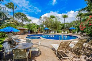 una piscina con sedie, tavoli e ombrelloni blu di Waikomo Stream Villas 132 a Koloa