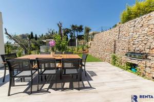 uma mesa de madeira com cadeiras pretas e uma parede de pedra em Cannes Hills Lovely Villa Pool & Garden em Le Cannet