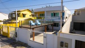 a house with a balcony with two chairs on it at Casa Blanca Foguete 3 suítes Praia Lagoa SPA aquecido Piscina in Cabo Frio