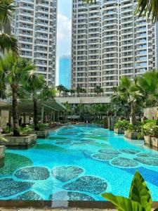 Cozy Studio Suite in Taman Anggrek Residences في جاكرتا: مسبح ازرق كبير بالنخيل والمباني