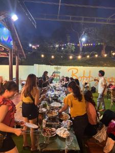 un grupo de personas de pie alrededor de una larga mesa con comida en BobbyFarm en Buôn Buk So (1)