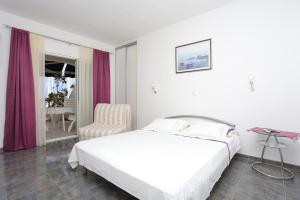a white bedroom with a bed and a chair at Apartments by the sea Sumpetar, Omis - 18286 in Jesenice