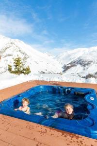 dwoje dzieci pływających w wannie z hydromasażem na śniegu w obiekcie BAITA NOEMI w Livigno