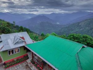 a house with a green roof with mountains in the background at 3 Sisters' Homestay in Ravangla