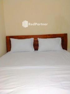 1 cama con 2 almohadas blancas y un cartel de socio rojo en la pared en Navisha Guest House Syariah near Exit Tol Batang RedPartner en Pekalongan