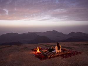 a woman sitting on a blanket next to a tent in the mountains at Grand Mercure Petra in Wadi Musa