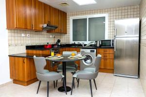 Two Continents Holiday Homes - Sea & Palm View Elegant 1 Bedroom Apartment في دبي: مطبخ مع طاولة وكراسي وثلاجة
