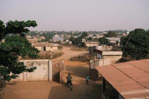 a person riding a bike down a dirt road in a village at Studio tout équipé au sein de l'ONG Okouabo in Parakou