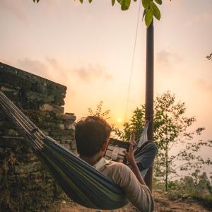 a man sitting in a hammock with a book at First Man Of Kasar Ram Singh Mehra Homestay in Almora