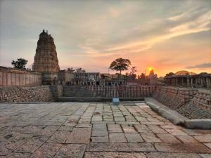 um pôr-do-sol sobre um templo com o pôr-do-sol no fundo em Sudhaahomestay em Hampi