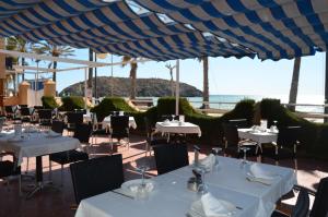 a restaurant with white tables and chairs and the ocean at Hotel Playa Grande in Puerto de Mazarrón