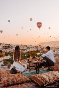 mężczyzna i kobieta siedzący przy stole obserwujący balony z gorącym powietrzem w obiekcie Hera Cave Suites w Göreme
