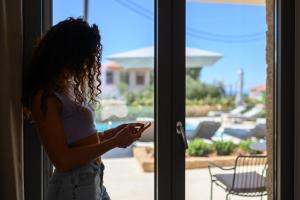 uma jovem a olhar pela janela para o telemóvel em Kannas Luxury Suites Mani em Stoupa