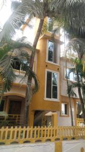 a yellow house with palm trees in front of it at Rosean Homestay Self Service Apartments in Candolim