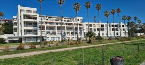 een wit gebouw met palmbomen ervoor bij Point Village Accommodation - Santos 57 in Mosselbaai